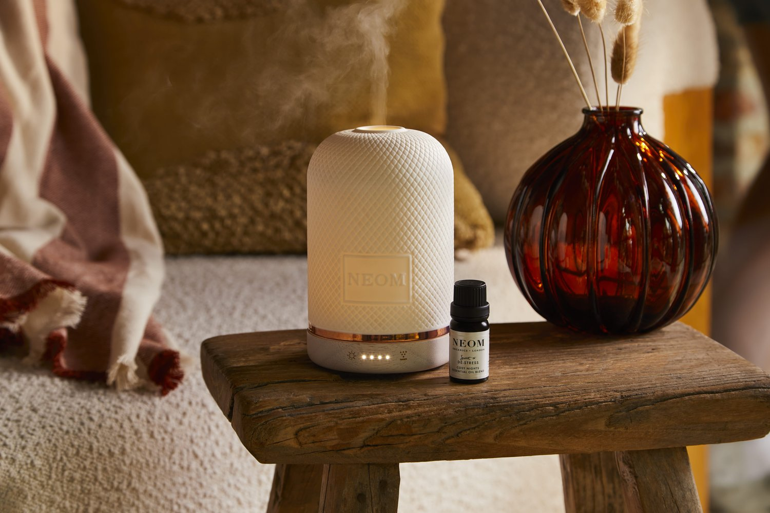 Cosy shot of the Neom diffuser alongside a vase of dried flowers and cosy armchair